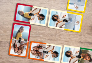 Eigene Domino Karten mit Fotos gestalten und drucken. Selbst gestaltete Domino-Karten mit Bildern von jungen Menschen liegen aneinader gereiht auf einem Holztisch.