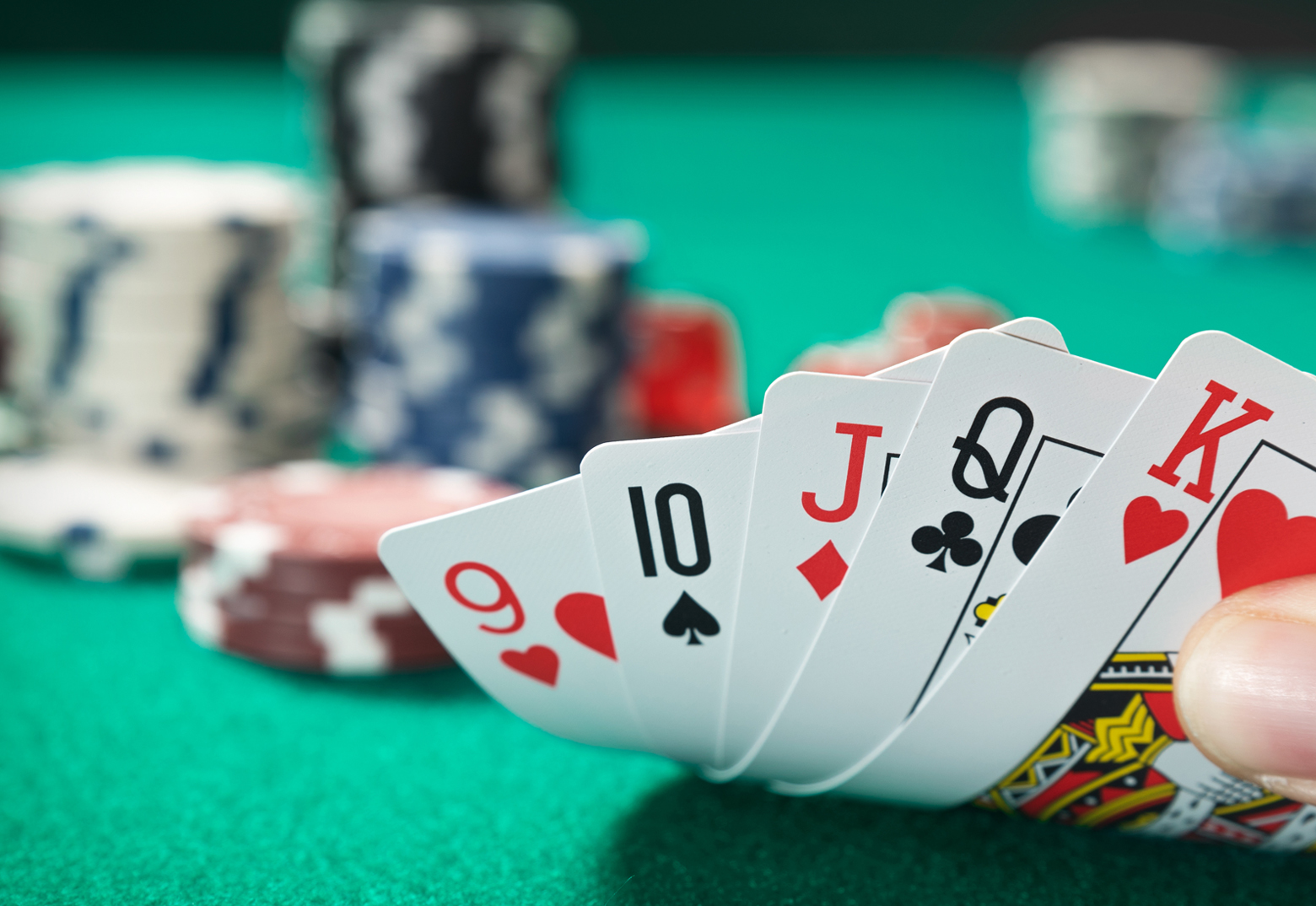 Aufgedeckte Pokerkarten sind in einer Hand zu sehen. Im Hintergrund stehen Poker Chips und der Pokertisch.