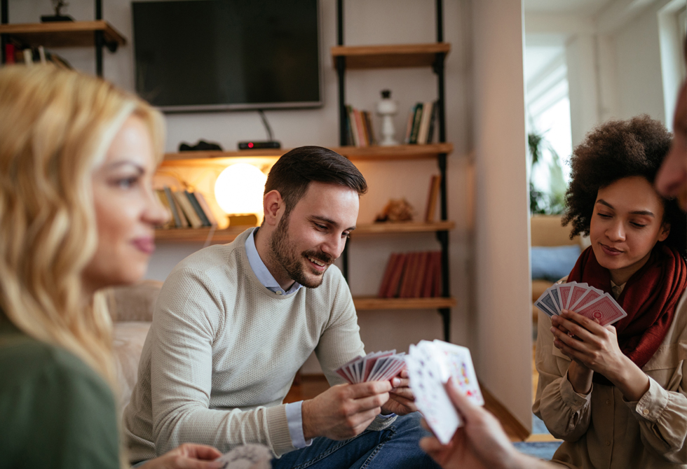 Vier Freunde sitzen im Wohnzimmer in einer Runde und spielen Doppelkopf