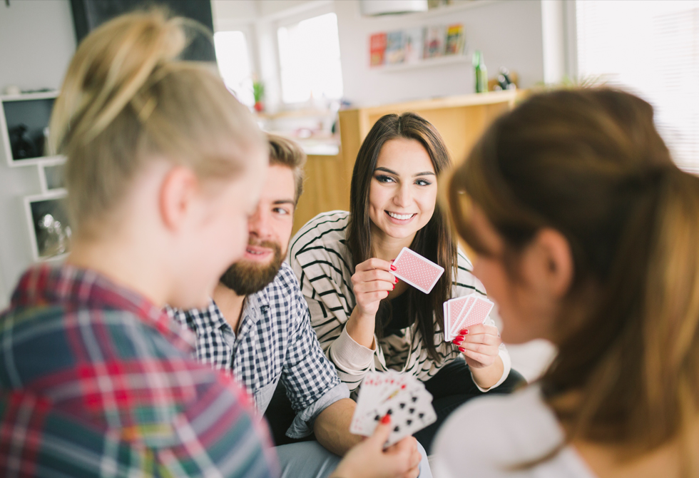 Drei Frauen und ein Mann spielen Karten und sind gut gelaunt