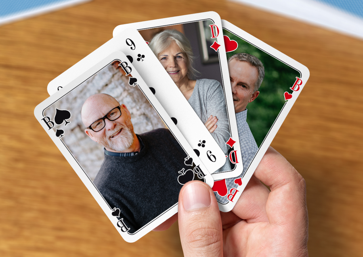 Doppelkopf-Karten selbst gestalten und drucken. Männerhand hält vier individuell gestaltete Doppelkopf-Karten zwischen dem Daumen und dem Zeigefinger