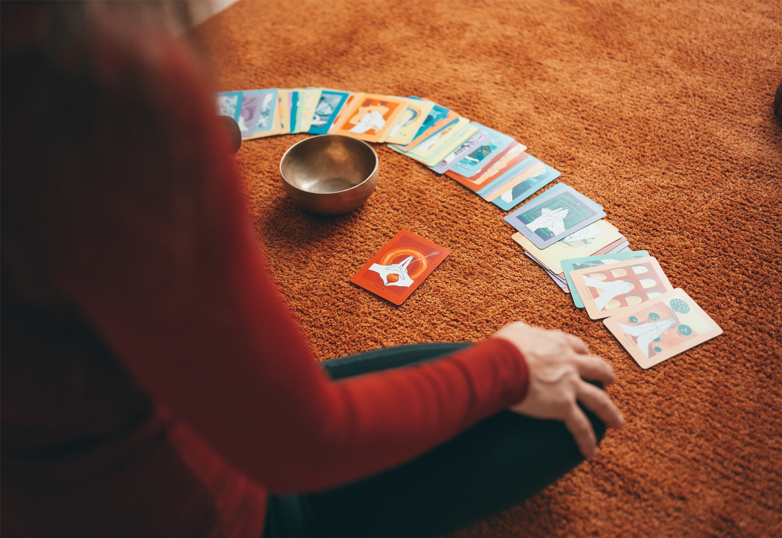 Eine Frau sitzt auf einem Orangen Teppich und hat Karten mit individuellen Motiven in einem Bogen ausgelegt