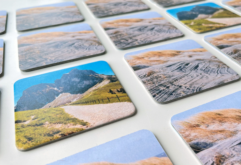 Nahaufnahme von selbst gestalteten Memo-Spielkarten, die auf einem weißen Tisch liegen. Es sind Urlaubsbilder darauf zu sehen.