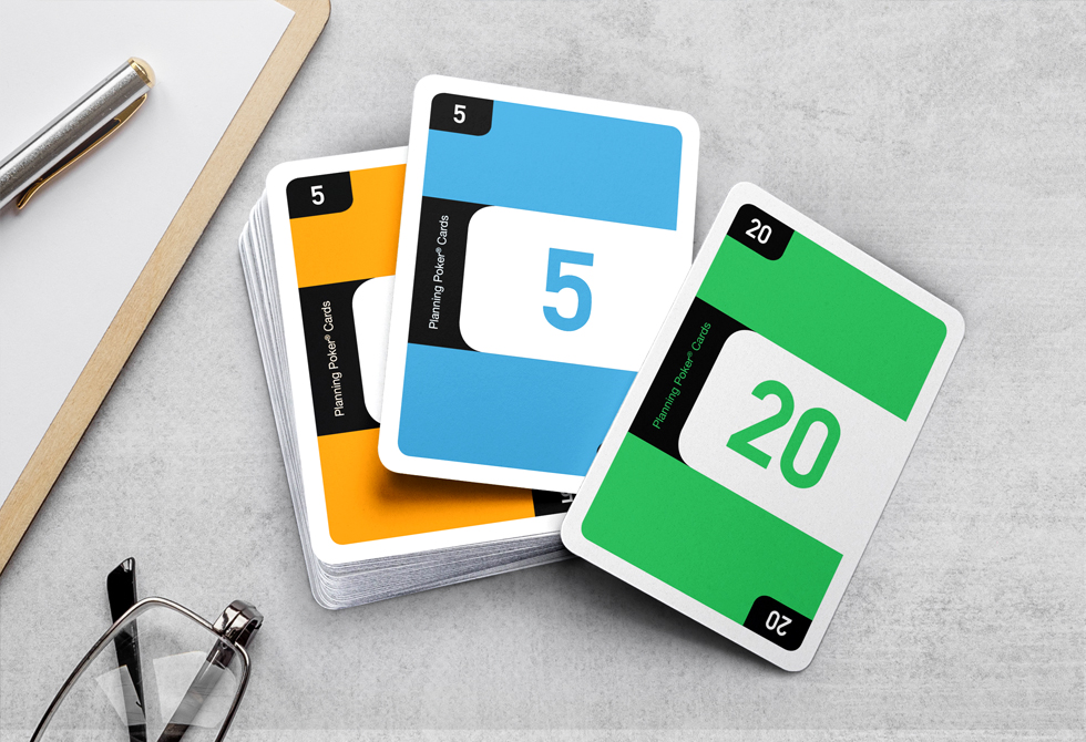 Auf einem Schreibtisch liegen drei aufgedeckte Planning Poker Karten in den Farben orange, blau und grün.