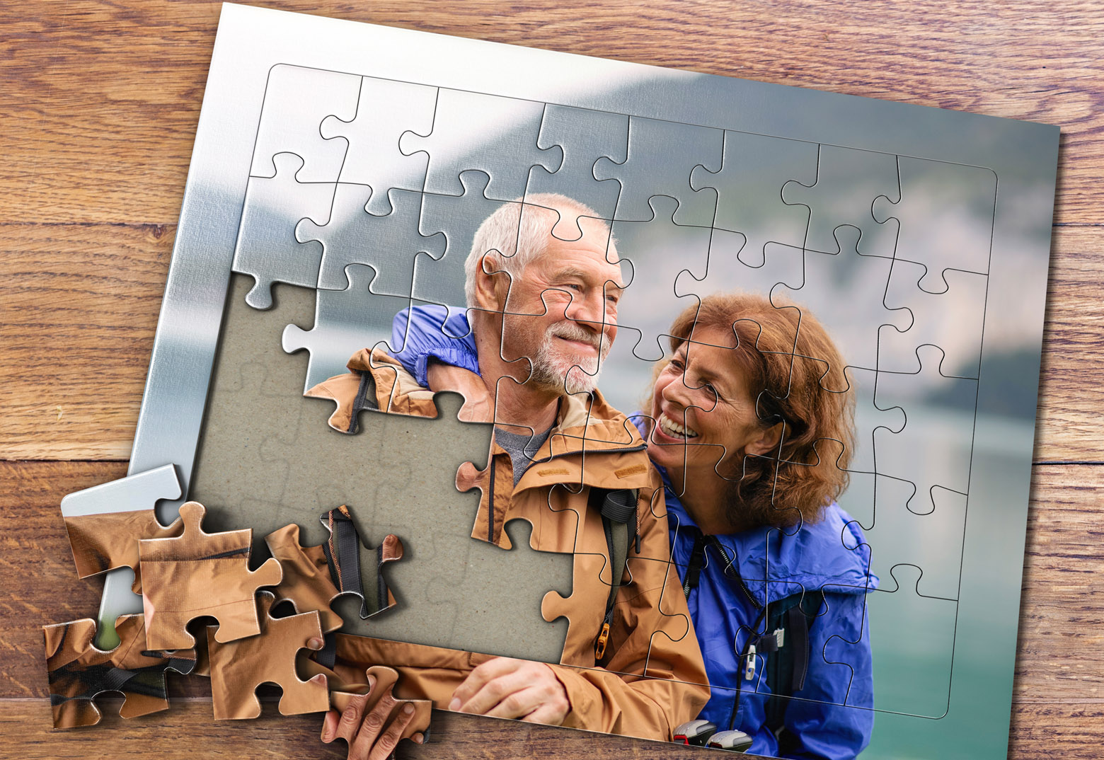 Auf einem Holztisch ist ein individuell gestaltetes Fotopuzzle bei MeinSpiel mit einem Paar, fotgrafiert beim Wandern vor einem See, als Motiv zu sehen