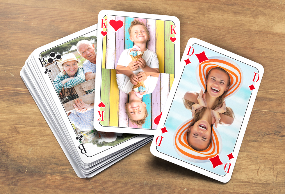 Poker-Karten selbst gestalten und drucken bei MeinSpiel. Poker-Karten mit eigenen Bildern liegen aufgedeckt auf einem Holztisch.