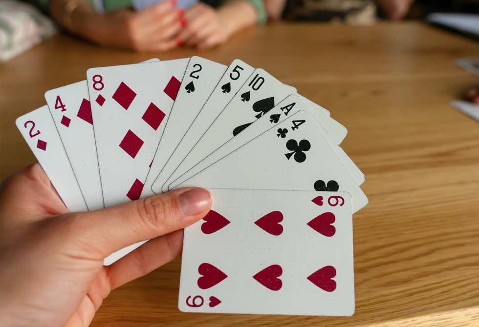 Frau hält Rommé Spielkarten in der Hand - Canasta Regeln erklärt