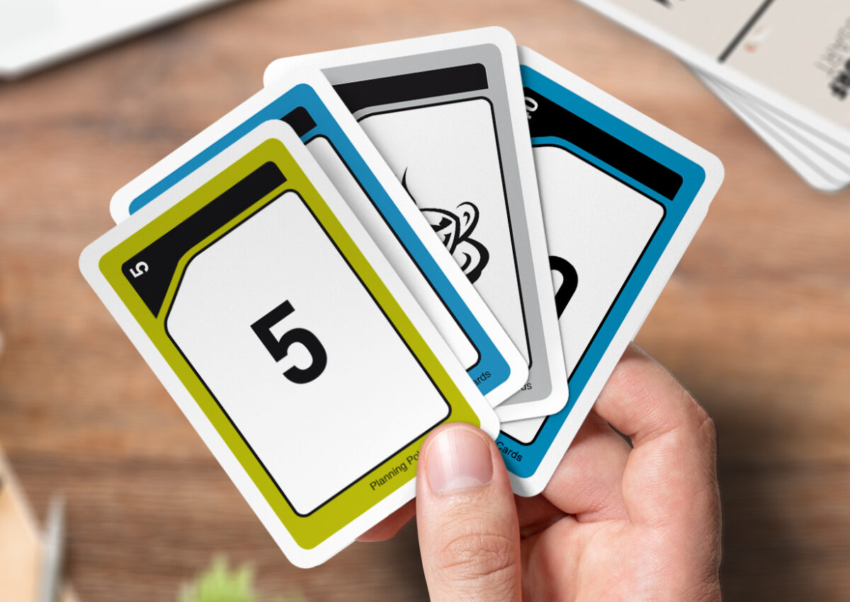 Eine Männerhand hält vier Planning Poker Karten, gestaltet bei MeinSpiel, zwischen dem Daumen und dem Zeigefinger