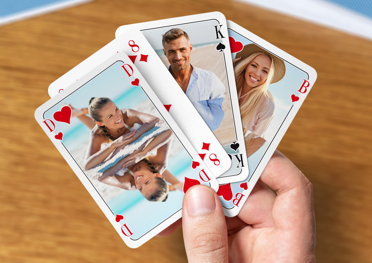 Eine Männerhand hält vier individuell gestaltete Poker-Karten - französisches Blatt - zwischen dem Daumen und dem Zeigefinger