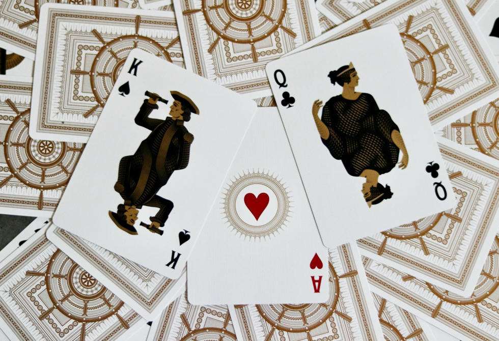 Drei selbst gestaltete Spielkarten, Dame, König, Ass liegen aufgedeckt auf zahlreichen nicht aufgedeckten Karten