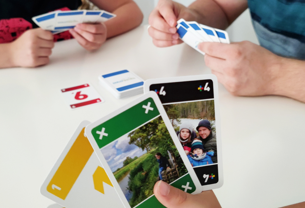 3 Personen spielen ein individuell gestaltetes MEINO Kartenspiel an einem weißen Tisch