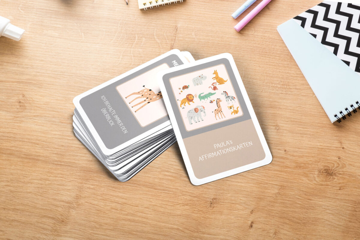Zwei selbst gestaltetete Affirmationskarten für Kinder liegen auf einem Holztisch