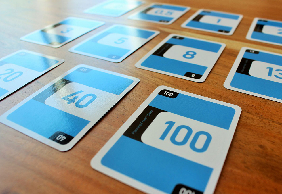Auf dem Holztisch liegen blaue Planning Poker Karten mit unterschiedlichen Zahlenwerten.