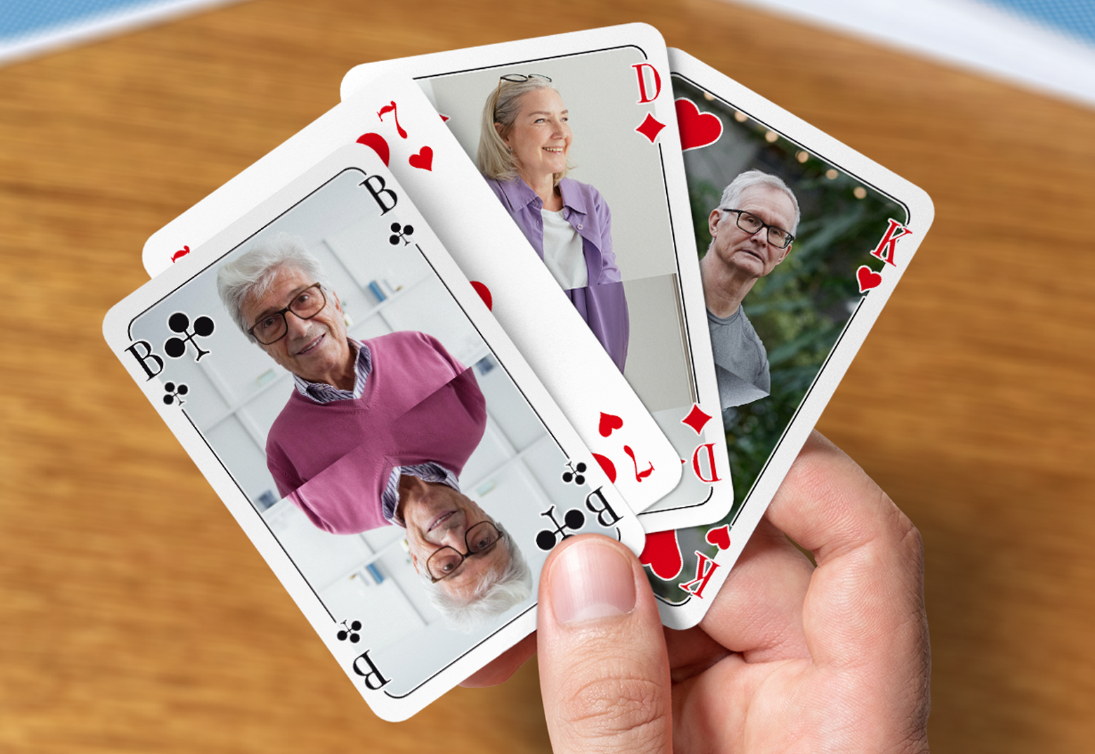 Eine Männerhand hält vier individuell gestaltete Skat-Karten mit Bildern von Freunden zwischen dem Daumen und dem Zeigefinger